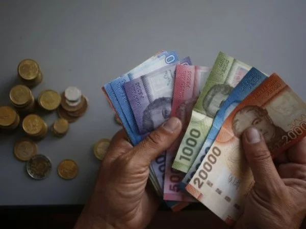 Persona sostiene billetes y monedas chilenas