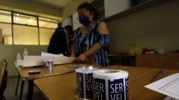 Vocal de mesa revisando un documento junto a pegatinas del Servel.