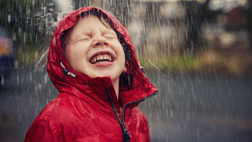 Un niño sonriendo bajo la lluvia.