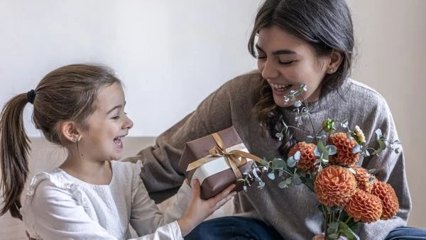 Nina entregándole un regalo y flores a su mamá.