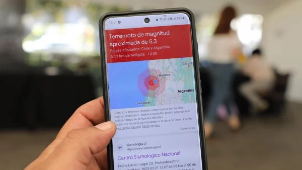 Foto de una mano sujetando un teléfono, en el que se lee la magnitud de un sismo registrado en Chile.