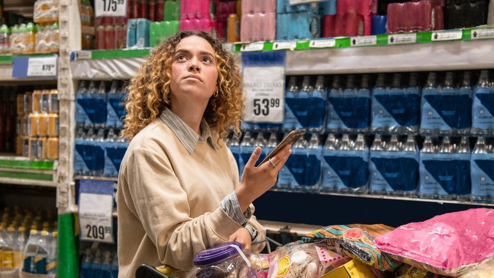 Una mujer camina por un supermercado con su carrito, mirando los anaqueles.
