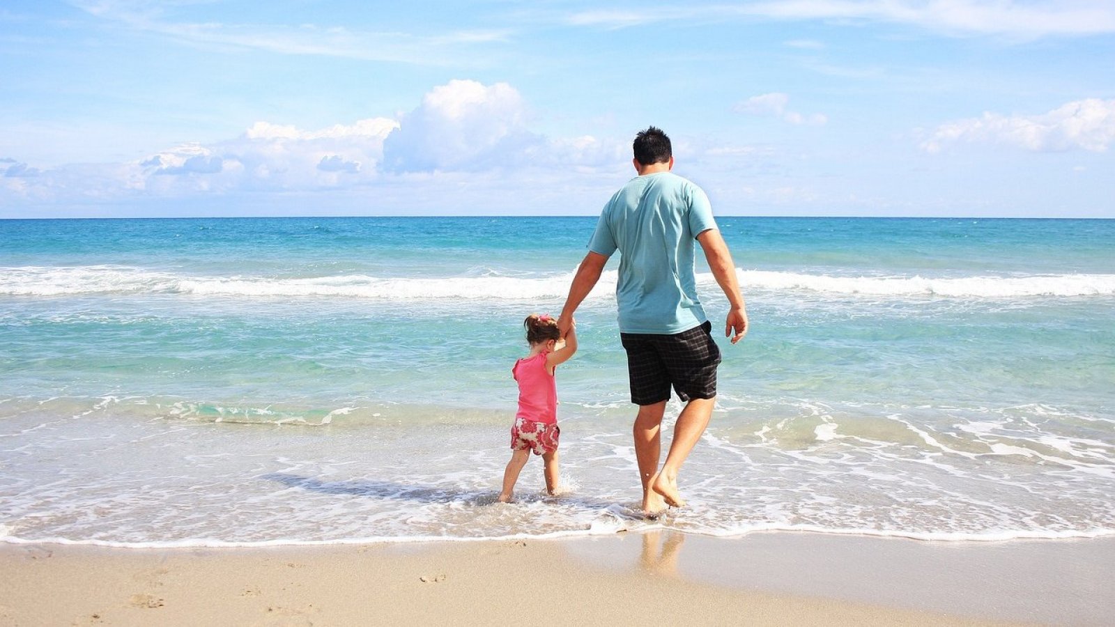 Padre e hija caminando por la orilla de la playa