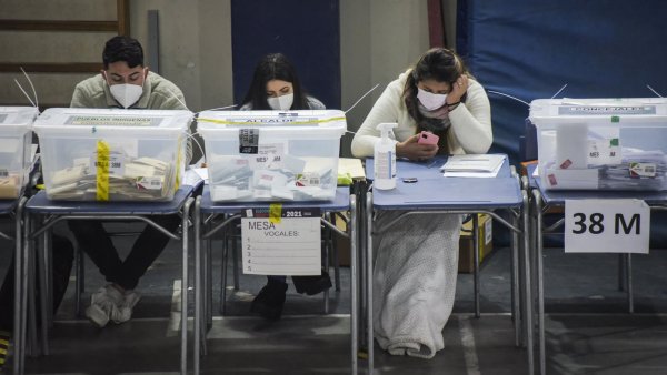 Tres personas sentadas, desempeñándose como vocales de mesa, en una mesa receptora de sufragios.