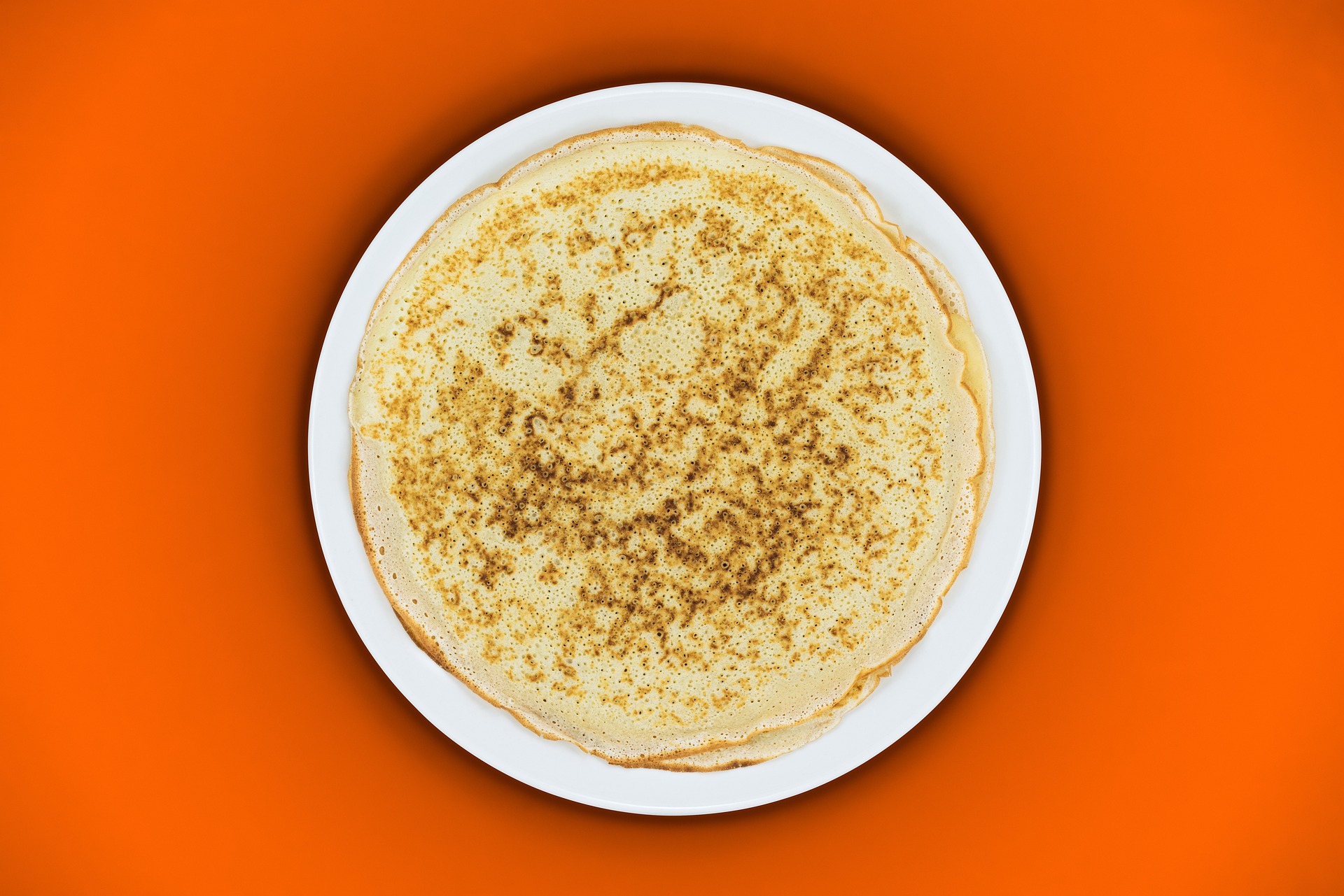 Panqueques sobre un plato blanco y un fondo naranja.
