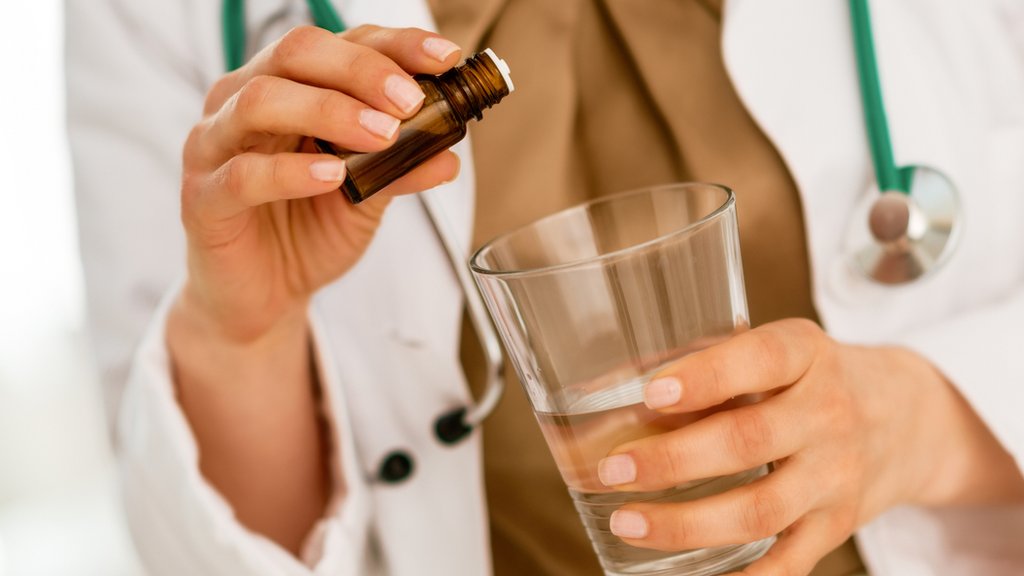 Manos de doctora echando estracto en vaso de agua
