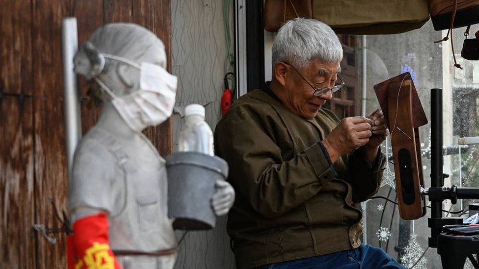 Hombre mayor cosiendo una billetera en la calle en China