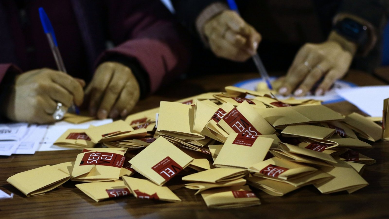 Manos en una mesa de votación con votos.