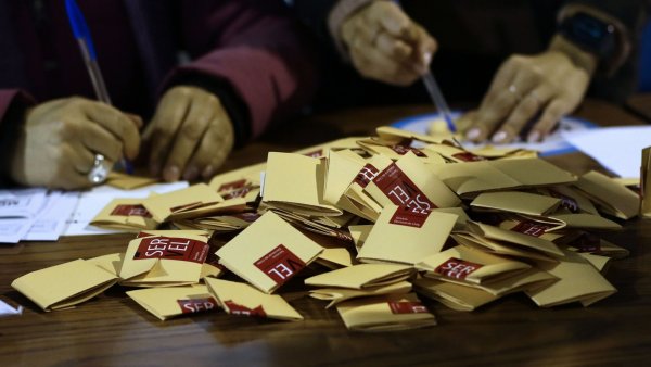 Manos en una mesa de votación con votos.
