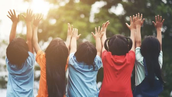 Cinco niños de espalda con sus manos arriba.