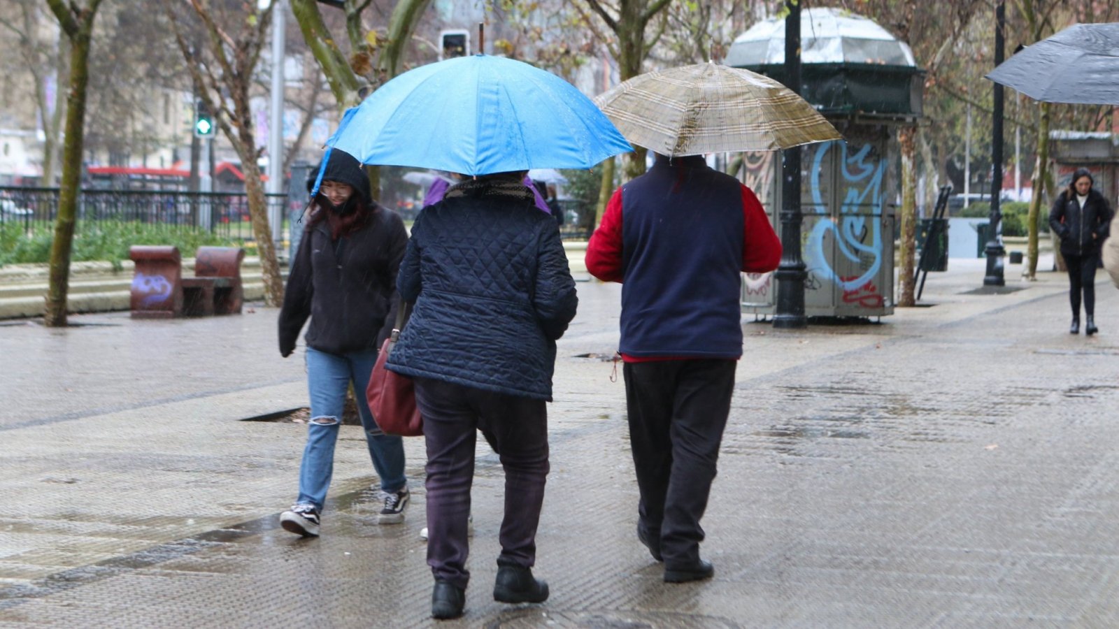Personas bajo la lluvia en Santiago y caminando con paraguas.