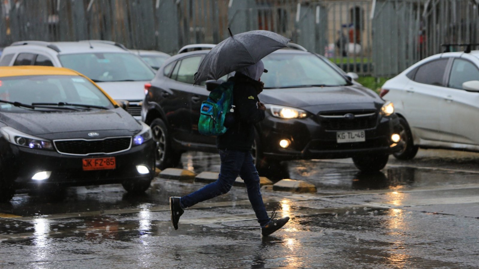 Persona con paraguas cruzando la calle con lluvia.
