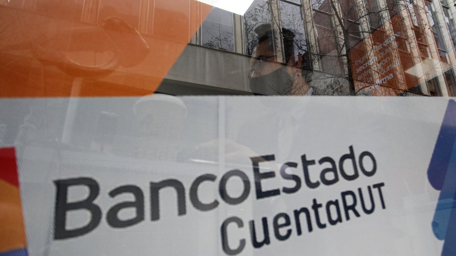 Persona en cajero automático de BancoEstado, mientras es cubierto por un ventana con publicidad de CuentaRUT