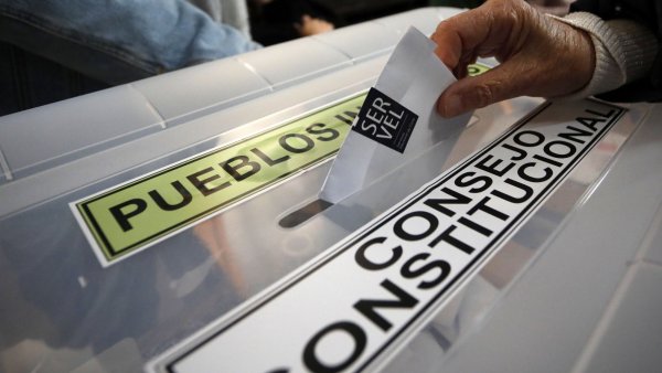 Mano ingresando voto en una urna electoral, en donde se lee 