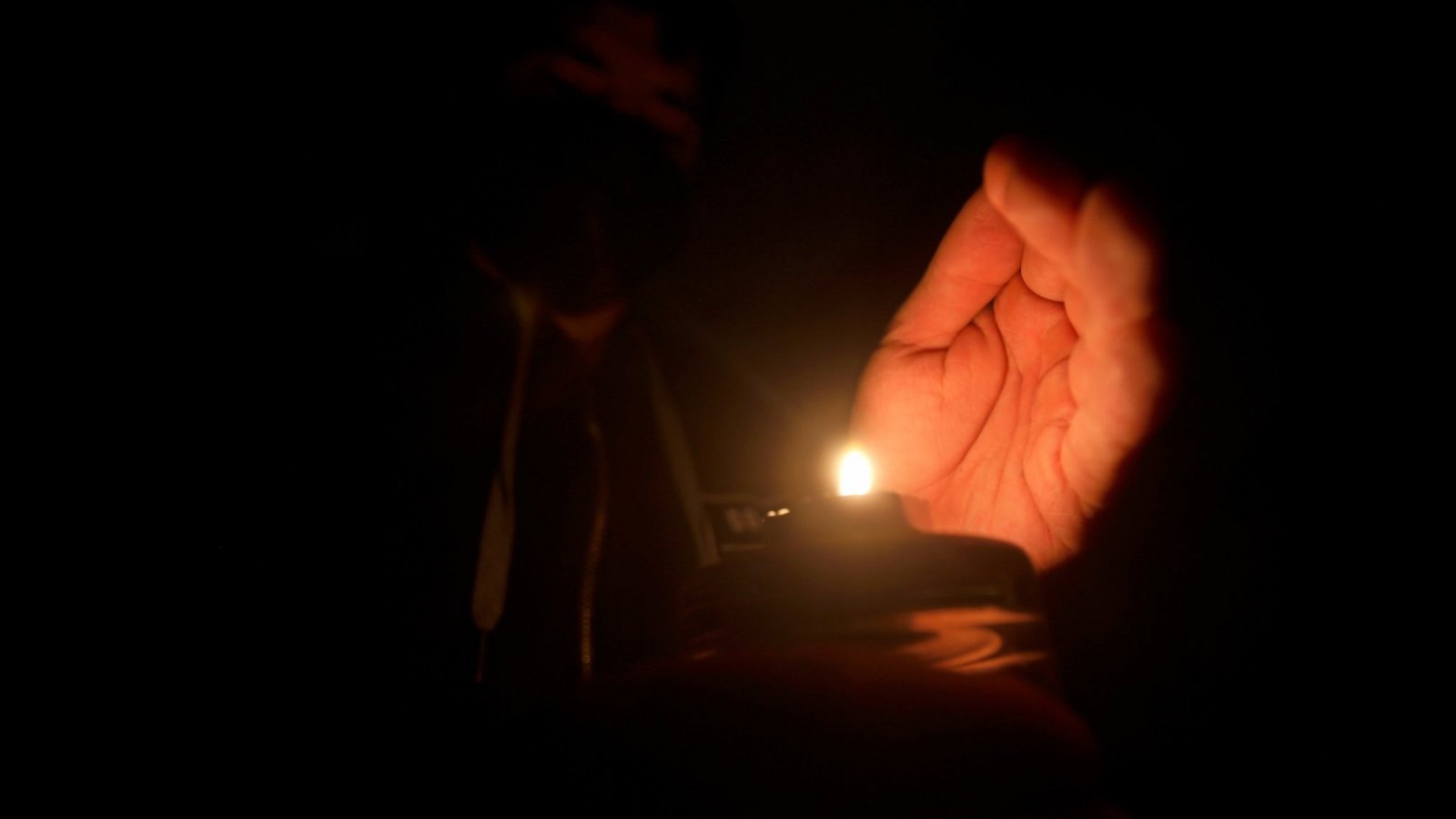 Persona sujetando una vela encendida en la oscuridad.