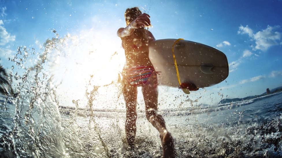 Mujer entrando a la playa con una tabla de surf.