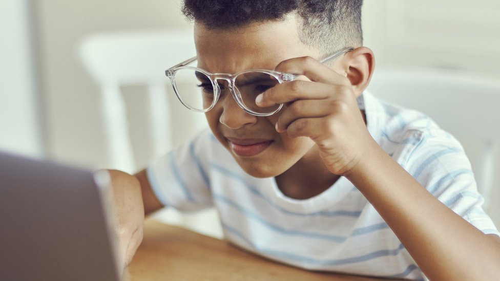 Un niño intenta ver la pantalla de un computador.