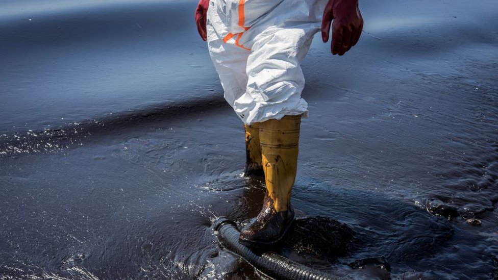 Un trabajador camina en agua contaminada por petróleo