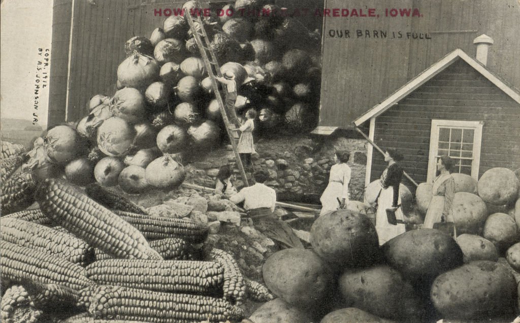Varias mujeres y un hombre están afuera de un granero, que está repleto de cebollas gigantes, maíz y papas, Waupun, Wisconsin, 1912.