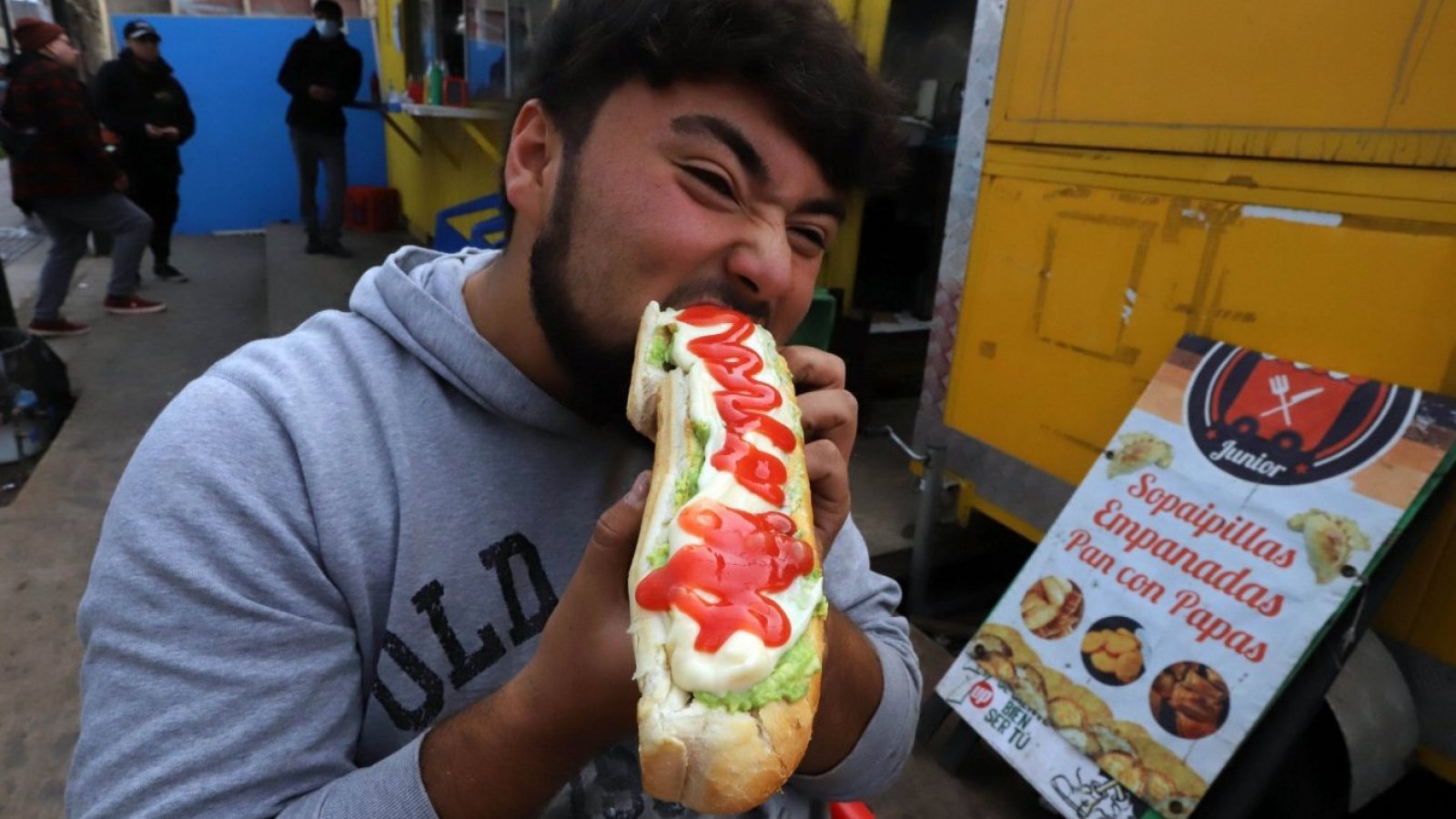 Joven comiendo un completo con ají.