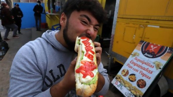 Joven comiendo un completo con ají.