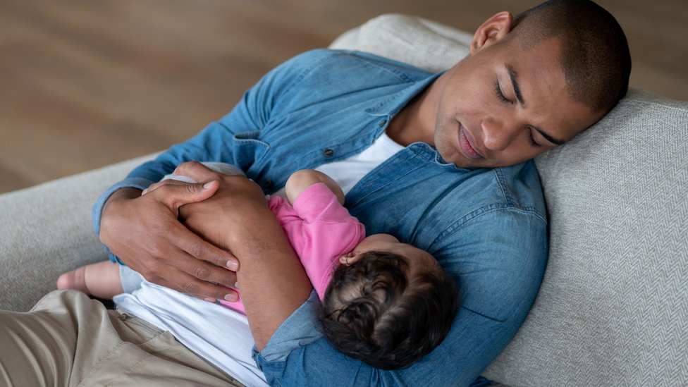 Padre dormido con su bebé en brazos.