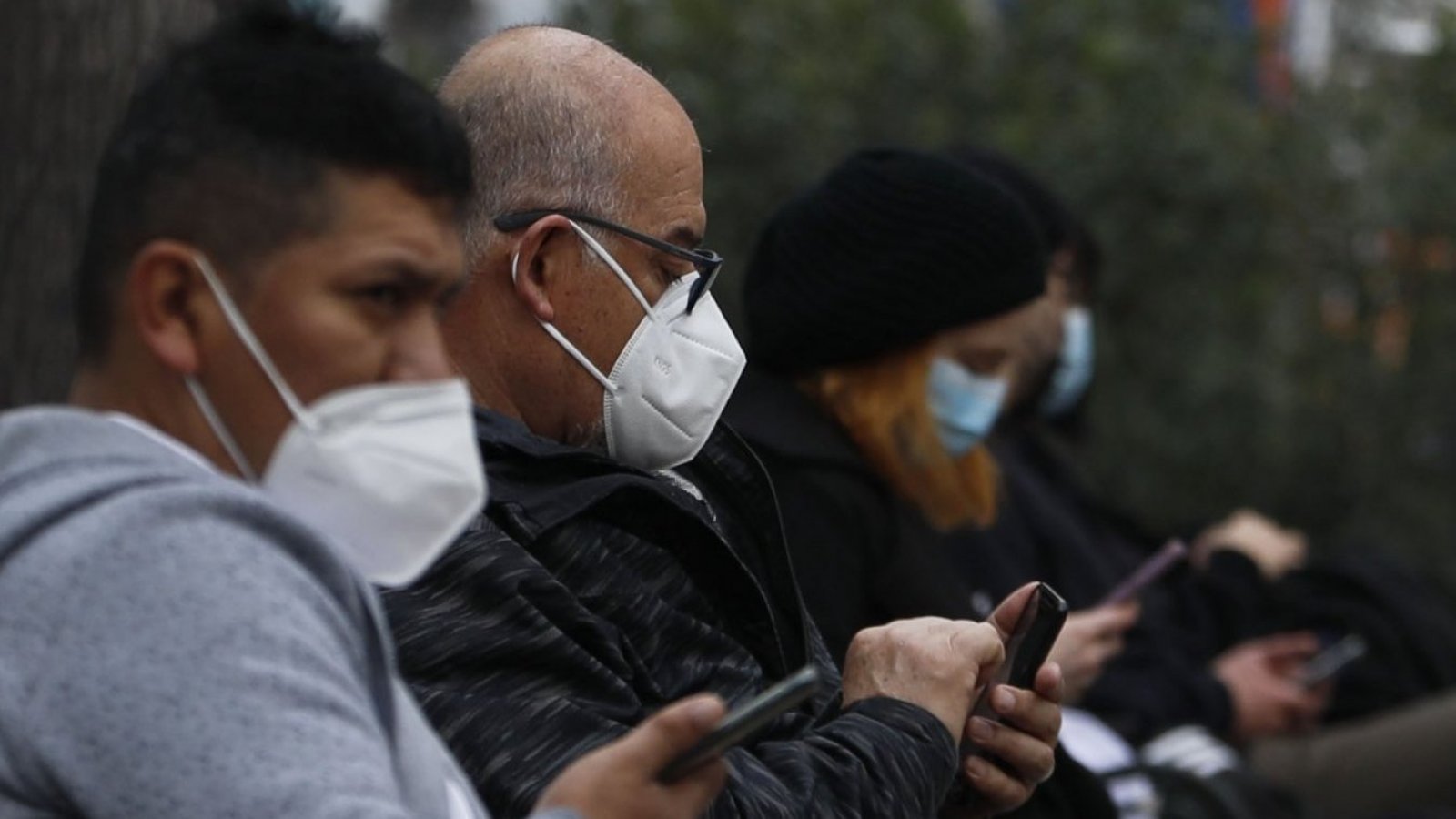 Personas con mascarilla revisando su celular.