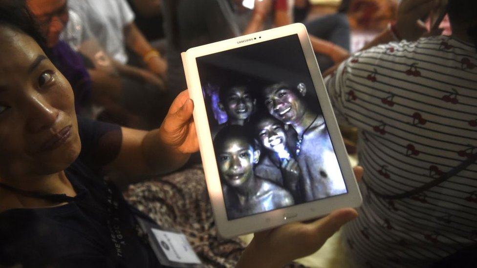 La madre de uno de los niños atrapados en la cueva de Tham Luang, en Tailandia, muestra una imagen de su hijo, dos amigos y el entrenador de fútbol.