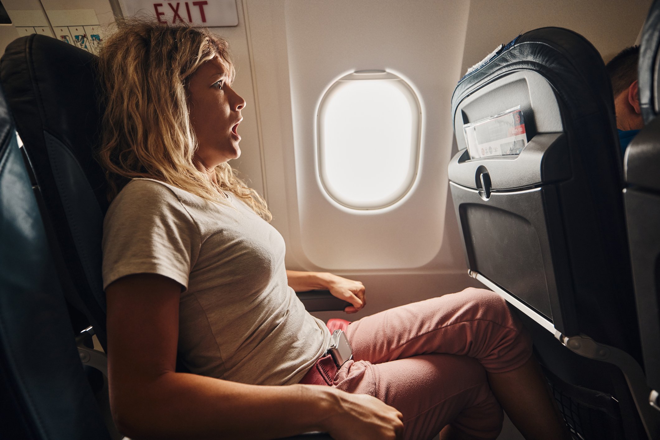 Mujer sujetada al asiento de un avión con cara de susto.