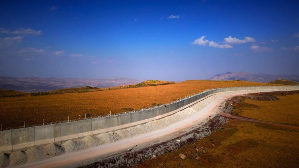 El muro fronterizo de hormigón corre a lo largo del paisaje con el cielo azul arriba