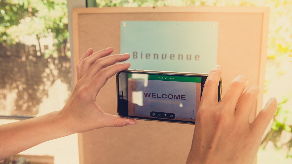 Un celular enfocando un cartel que dice Bienvenue y el celular traduce Welcome