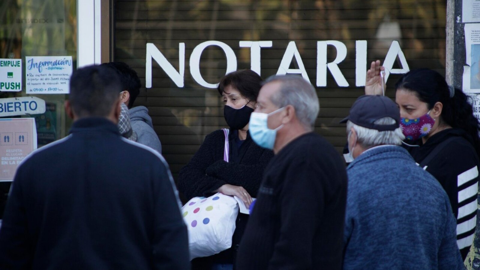 Personas haciendo fila fuera de una notaría.