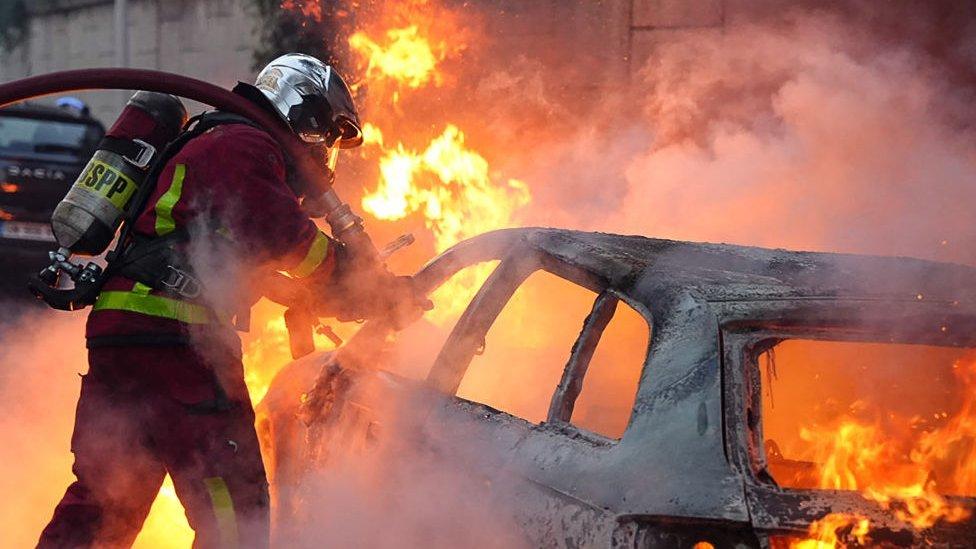 Un bombero intenta apagar un auto incendiado.