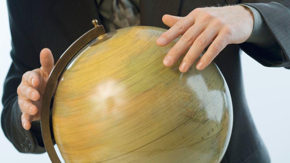 Hombre haciendo girar con sus manos un globo terráqueo