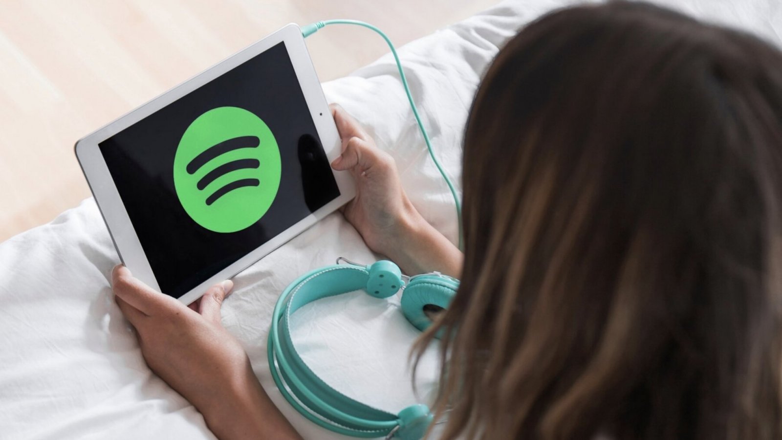 Mujer recostada en una cama escuchando Spotify en un tablet.