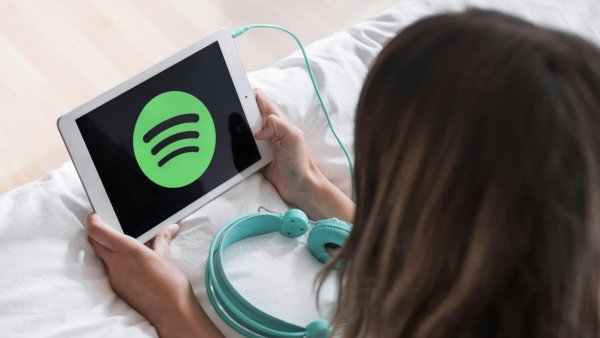 Mujer recostada en una cama escuchando Spotify en un tablet.
