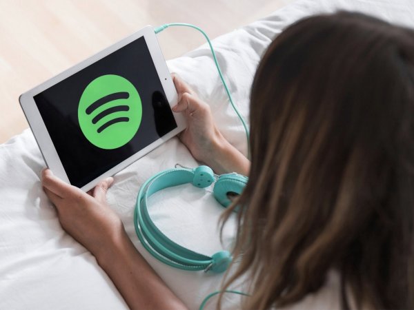 Mujer recostada en una cama escuchando Spotify en un tablet.