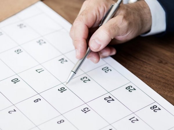 Mano revisando el calendario con un lápiz.