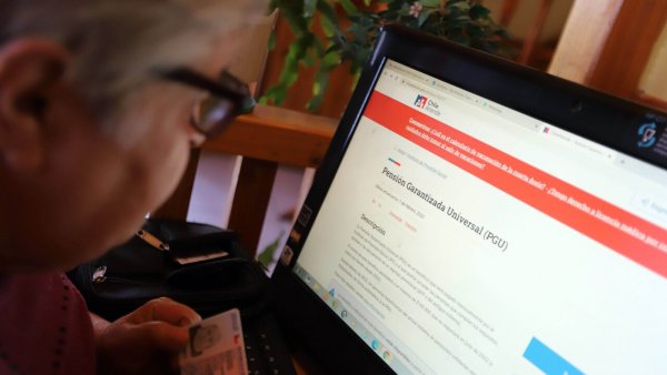 Persona mayor leyendo información de la PGU en un computador.