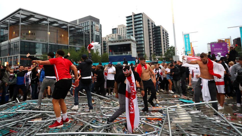 Aficionados de Inglaterra pisan vallas de seguridad fuera del estadio de Wembley.