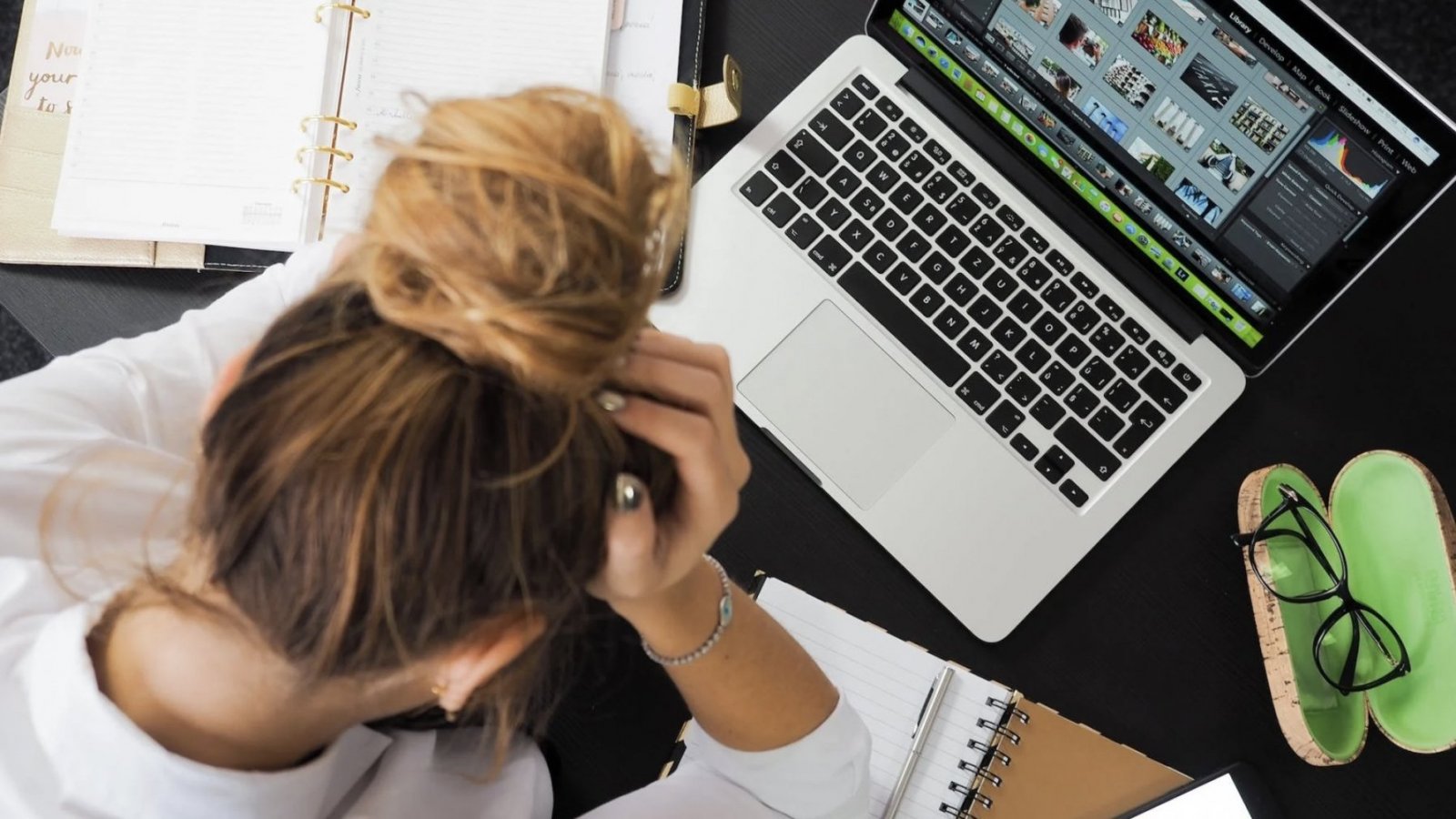 Mujer sentada frente a un computador con las manos en la cabeza.