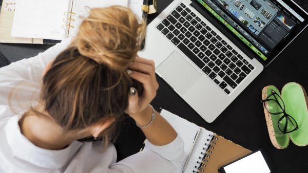 Mujer sentada frente a un computador con las manos en la cabeza.