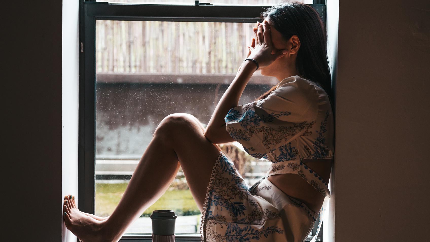 Una mujer sola se sienta frente a una ventana con las manos en la cara