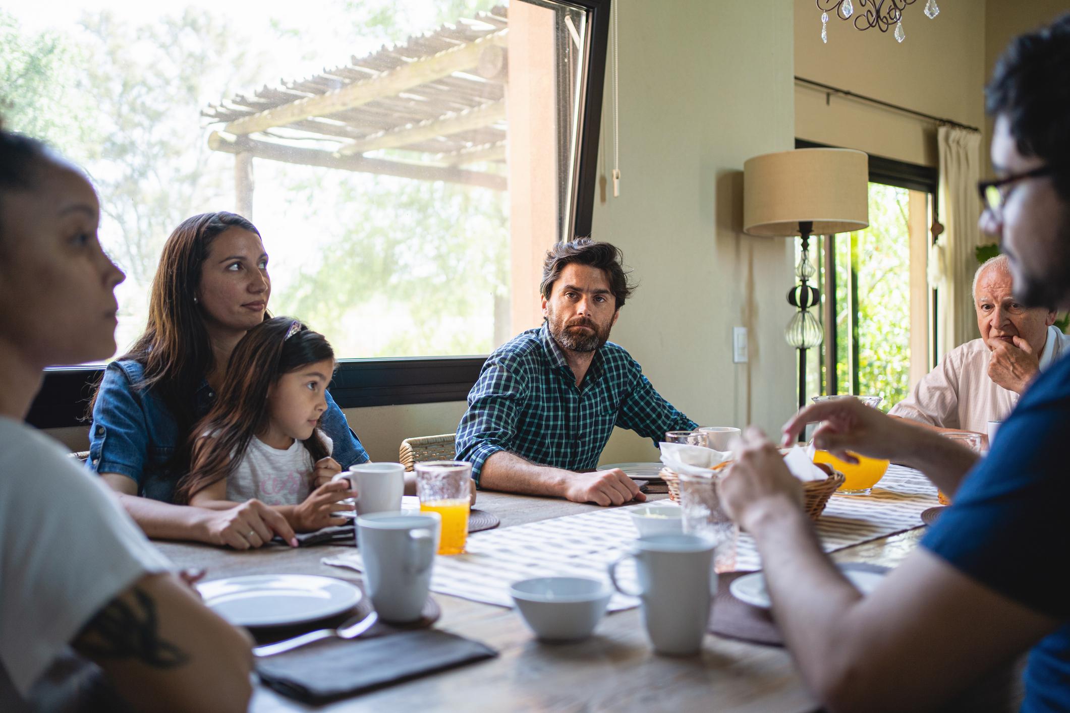 Una familia sentada en la mesa de la comida y uno de los hermanos observa a su hermana con recelo