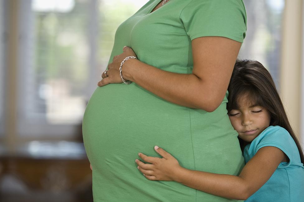 Una mujer hispana embarazada y su hija que la abraza