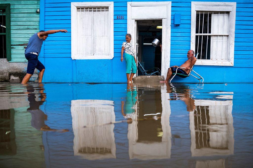 Una pareja afuera de su casa y otro hombre camina por el agua en una zona inundada de Batabanó, provincia de Mayabeque, Cuba.