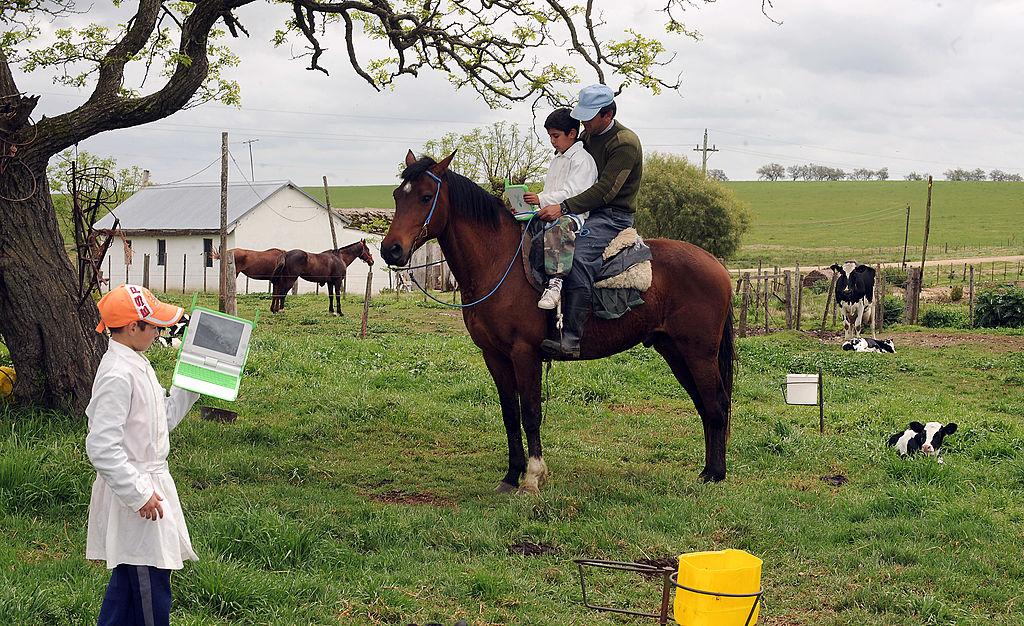 Un niño junto a un hombre adulto con una laptop arriba de un caballo y otro niño parado con otra laptop en las inmediaciones de una escuela rural en Uruguay. Foto de octubre de 2008.