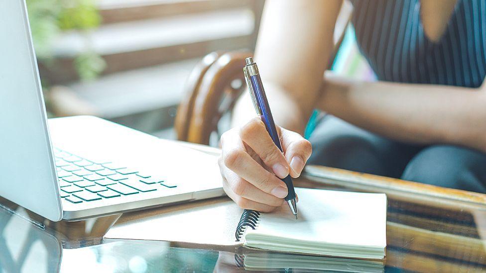 Mujer escribiendo a mano con un laptop al lado