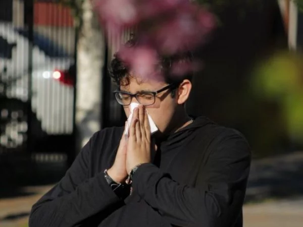 Hombre con pañuelo estornuda por resfrío o alergia