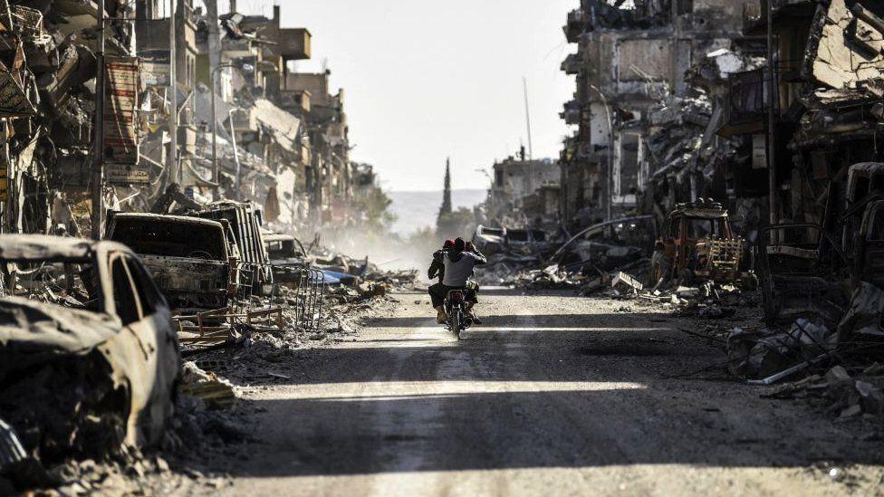 A Syrian youth uses his cell phone to film the destroyed vehicles and heavily damaged buildings down a street in Raqqa on October 20, 2017